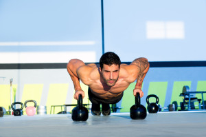 Mand træner armstrækninger med to sorte kettlebells